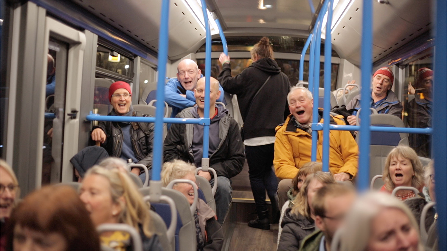 a group on people singing on a public bus as a passenger walks up the aisle